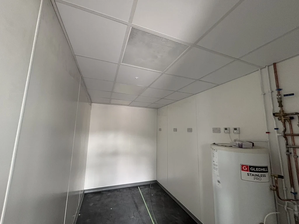 Service room with white wall panels, suspended ceiling panels and visible equipment and pipework