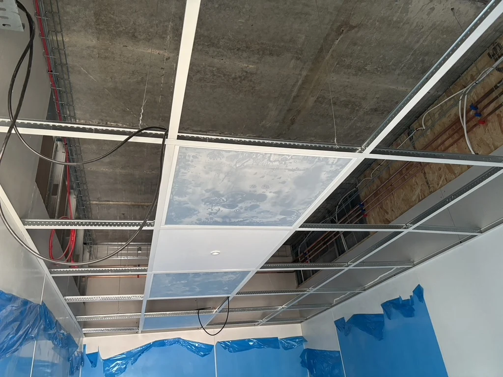 Part-installed suspended ceiling grid with some panels in place and visible cabling overhead